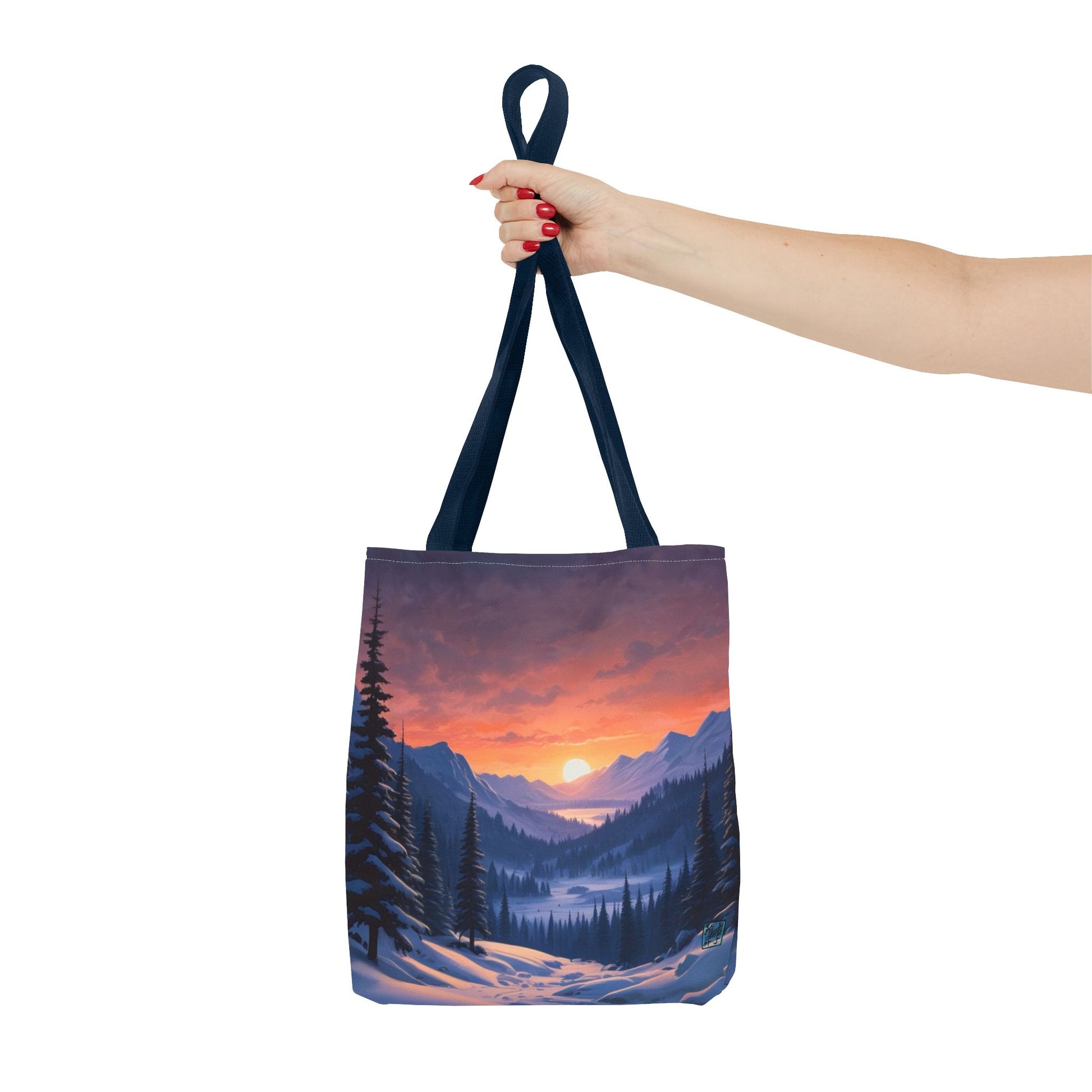 The Navy 16" x 16" Snow Valley Tote Bag has color matched handles and all around print. A woman's hand with red nail polish is grabbing the handles.Her arm is outstretched to the middle. The tote is against a white background.The design by Lee Hansheng Studios showcases a snowy hill/mountain area with large pine trees on both sides continuing into the horizon. The sun rises past the horizon consisting of yellow,orange,red hues illuminating onto wispy clouds,snowy field, mountains and dark green pine trees. 