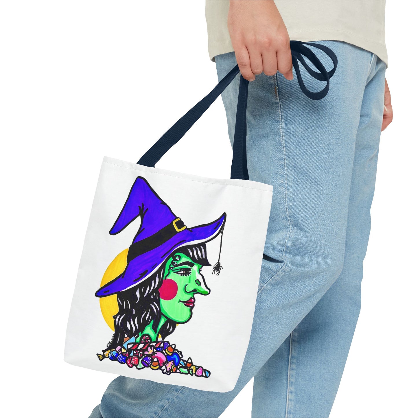 This is the Navy 13" x 13" Witch Tote Bag by Storm Garden Studio. The handles are color matched. It shows the side profile of a witch. She has a purple witch hat, a black belt on hat, yellow buckle, a spider crawling down the front, red rosy cheeks, red lips and assorted candy under the neck. Behind her is a bright yellow circle past her hair. A man's hand with a beige tee and light- colored jeans is grabbing the handles from the hip down. The tote is against a white background.