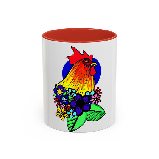 This it the Red 11 oz Cock Accent Coffee Mug by Storm Garden Studio. This image showcases the front of the mug. The illustration is of a rooster with a dark blue circular background. The rooster is adorned with flowers on the bottom of its neck. It is bright green, dark blue, yellow, orange and pink. The rooster is bright red and fades into yellow. The mug is against a white background. 