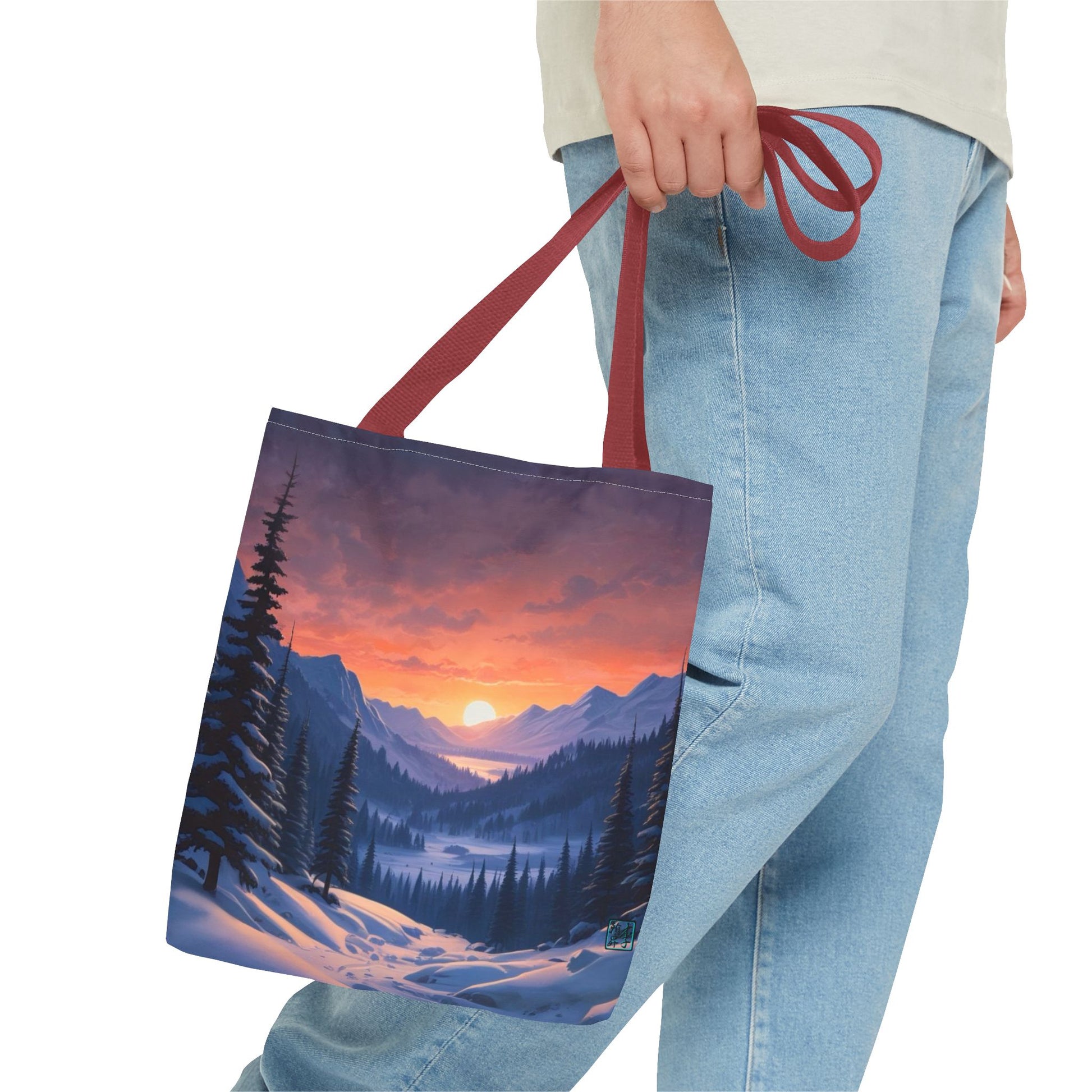 The Red 13" x 13" Snow Valley Tote Bag has color matched handles and all around print. A man's hand with a beige tee and light- colored jeans is grabbing the handles from the hip down. The tote is against a white background.The design by Lee Hansheng Studios showcases a snowy hill/mountain area with large pine trees on both sides continuing into the horizon. The sun rises past the horizon consisting of yellow,orange,red hues illuminating onto wispy clouds,snowy field, mountains and dark green pine trees. 