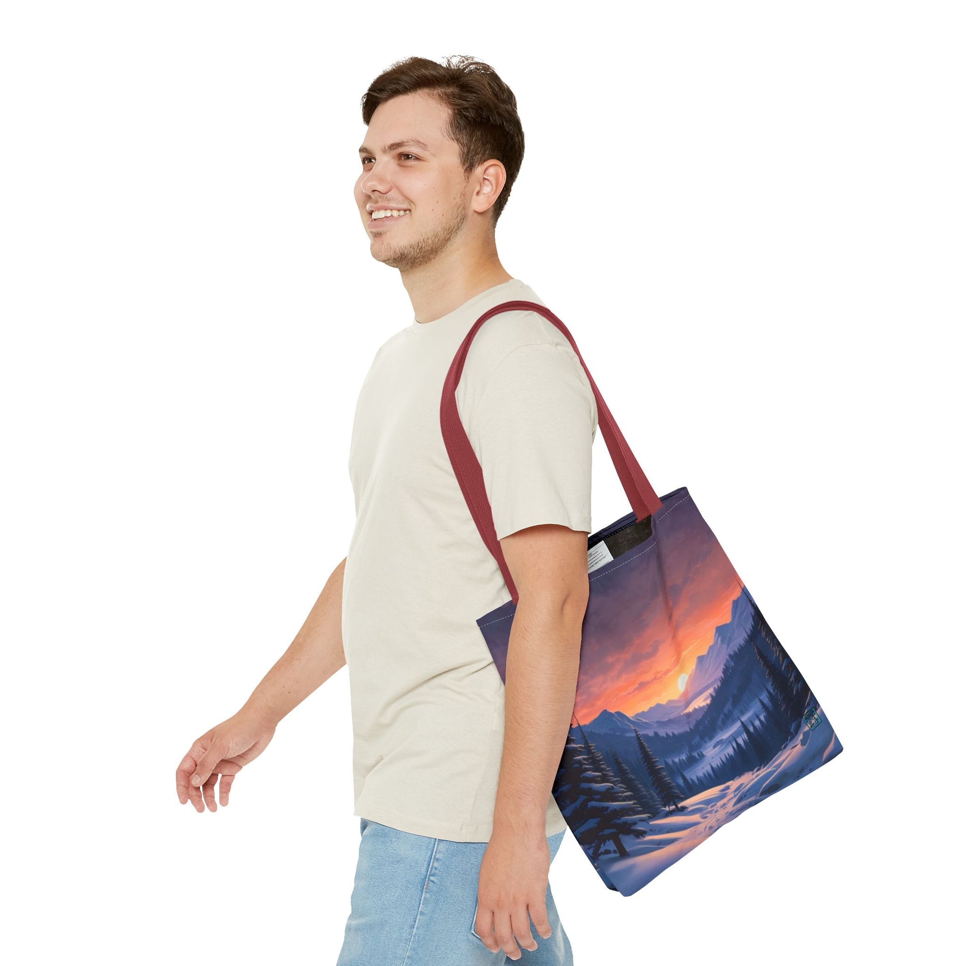 The Red 18" x 18" Snow Valley Tote Bag has color matched handles. A man with a smile, short wavy brown hair,beige tee plus jeans with tote around their shoulder and walking towards the left against a white background.The design by Lee Hansheng Studios showcases a snowy hill/mountain area with large pine trees on both sides continuing into the horizon. The sun rises past the horizon consisting of yellow,orange,red hues illuminating onto wispy clouds,snowy field, mountains and dark green pine trees. 