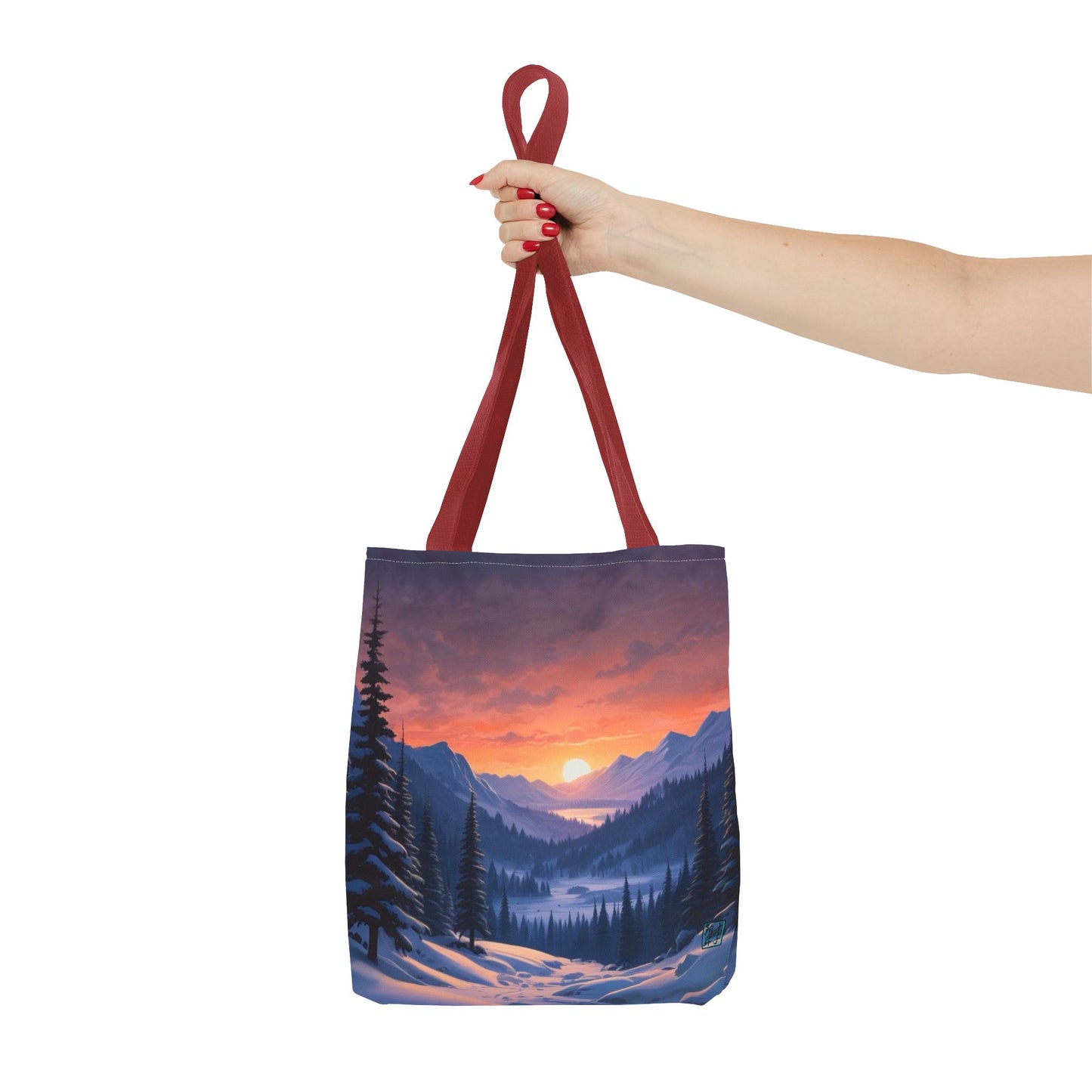 The Red 16" x 16" Snow Valley Tote Bag has color matched handles and all around print.A woman's hand with red nail polish is grabbing the handles.Her arm is outstretched to the middle. The tote is against a white background.The design by Lee Hansheng Studios showcases a snowy hill/mountain area with large pine trees on both sides continuing into the horizon. The sun rises past the horizon consisting of yellow,orange,red hues illuminating onto wispy clouds,snowy field, mountains and dark green pine trees. 