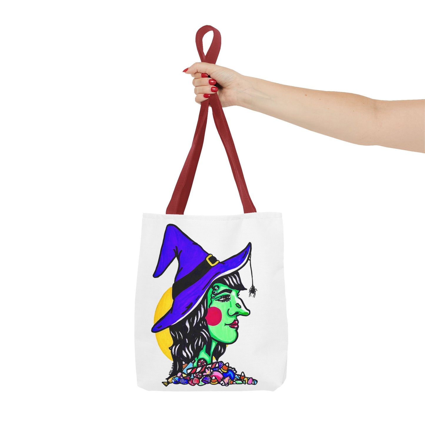 This is the Red 13" x 13" Witch Tote Bag by Storm Garden Studio.The handles are color matched.It shows the side profile image of a witch.She is facing the left side.She has a purple witch hat with a black belt, yellow buckle, a spider crawling down the front, red rosy cheeks, red lips and assorted candy under the neck.Behind her is a bright yellow circle past her hair.A woman's hand with red nail polish is grabbing the handles. Her arm is outstretched to the middle. The tote is against a white background.