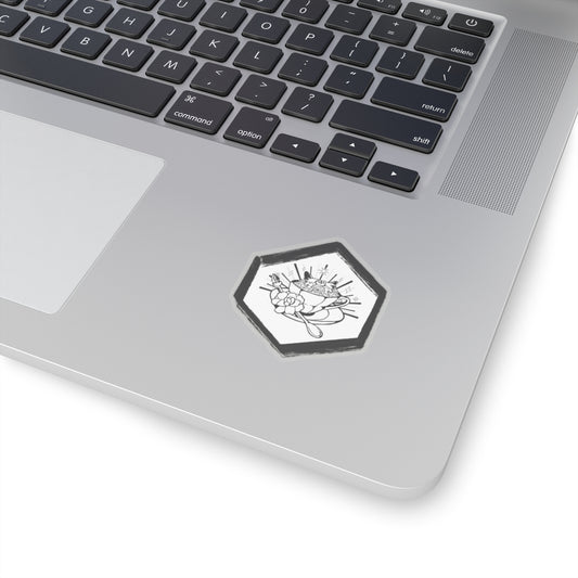 This is the Transpare 2" x 2" Hexagon Tidy Tea Witch Kiss-cut Sticker by Tidy Tea Witch.The sticker is white a black with hand painted like features on the border.In the middle is a teacup,a saucer and crystal spoon.There's a large flowering covering the spoon,flowers filling it to the fullest, stars and lines exploding in the background and cat ears popping out of cup. The sticker is a close up image on a gray laptop to the right of the gray mouse pad below the black keyboard with white printed letters.