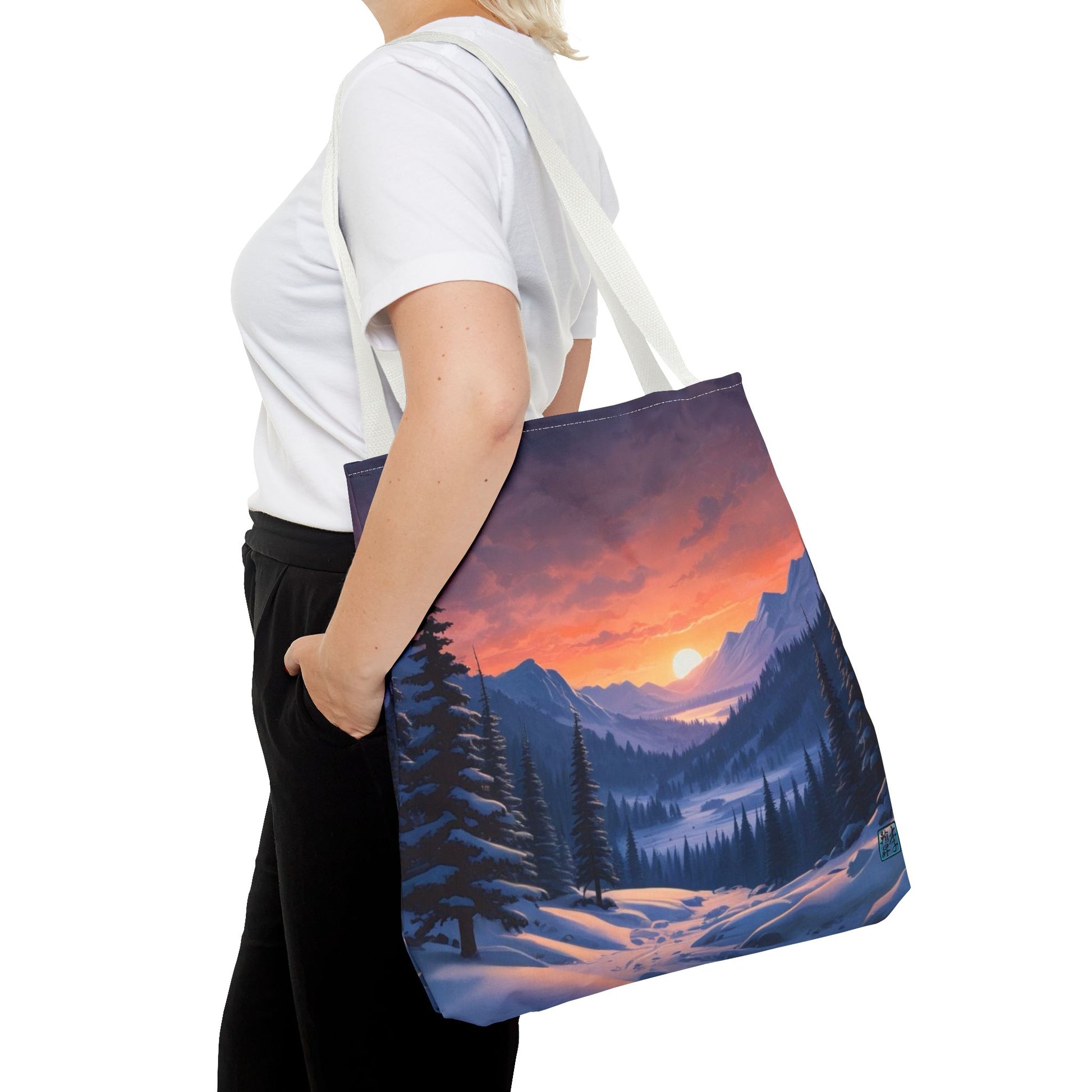 The White 18" x 18" Snow Valley Tote Bag has color matched handles. A lady with short blonde hair,white tee plus black pants with tote around their shoulder and hand in pocket against a white background.The design by Lee Hansheng Studios showcases a snowy hill/mountain area with large pine trees on both sides continuing into the horizon. The sun rises past the horizon consisting of yellow,orange,red hues illuminating onto wispy clouds,snowy field, mountains and dark green pine trees. 