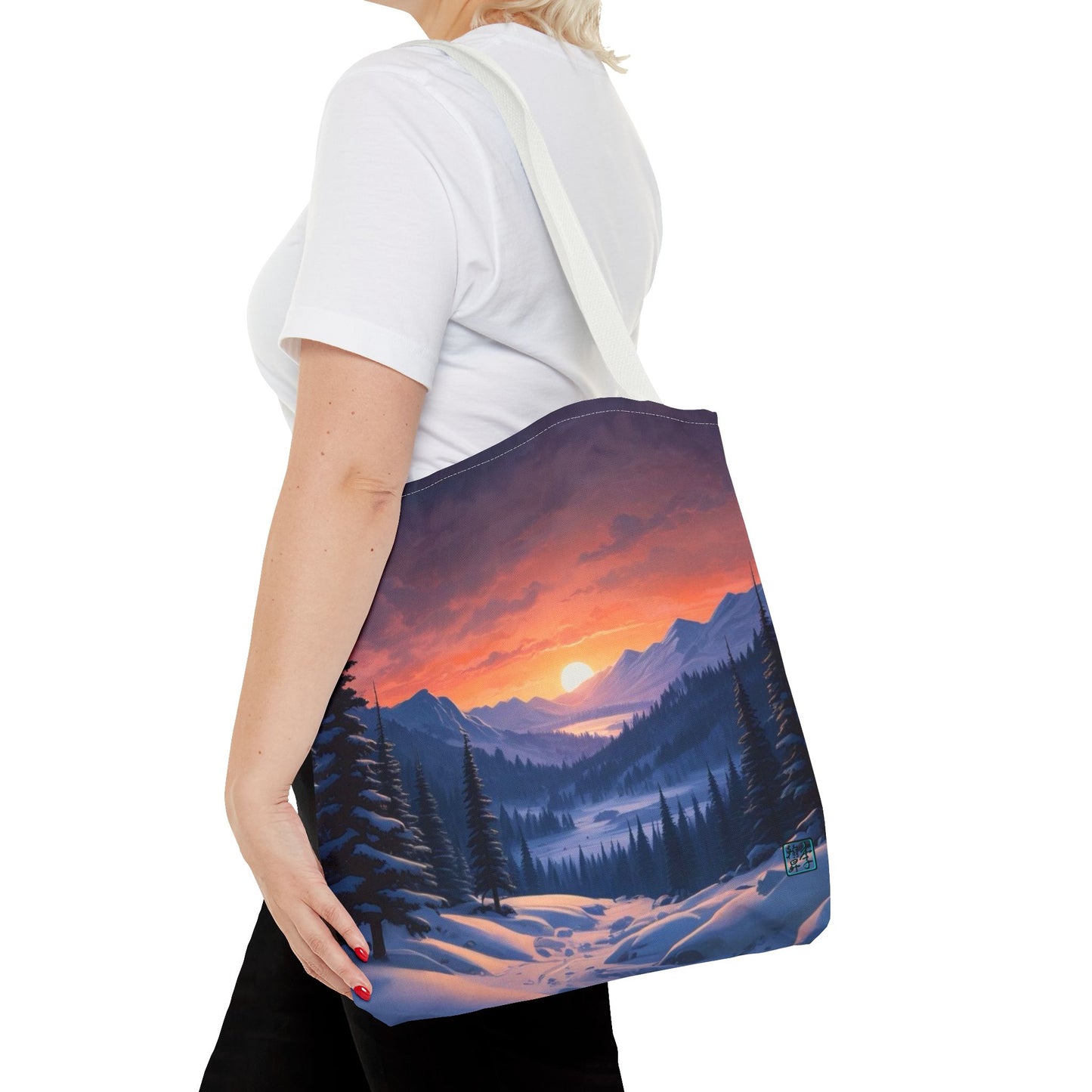 The White 16" x 16" Snow Valley Tote Bag has color matched handles. A lady with short blonde hair,white tee plus black pants with tote around their shoulder and hand in pocket against a white background.The design by Lee Hansheng Studios showcases a snowy hill/mountain area with large pine trees on both sides continuing into the horizon. The sun rises past the horizon consisting of yellow,orange,red hues illuminating onto wispy clouds,snowy field, mountains and dark green pine trees. 