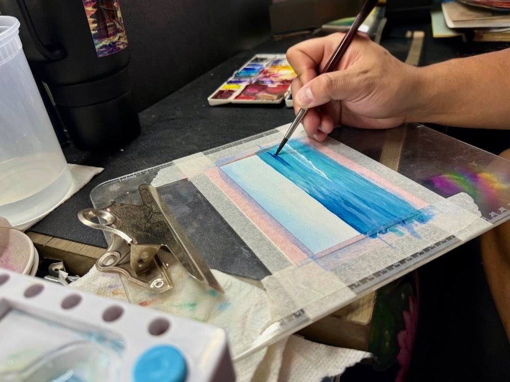 LHS painting on a watercolor paper with a brush, surrounded by art supplies.