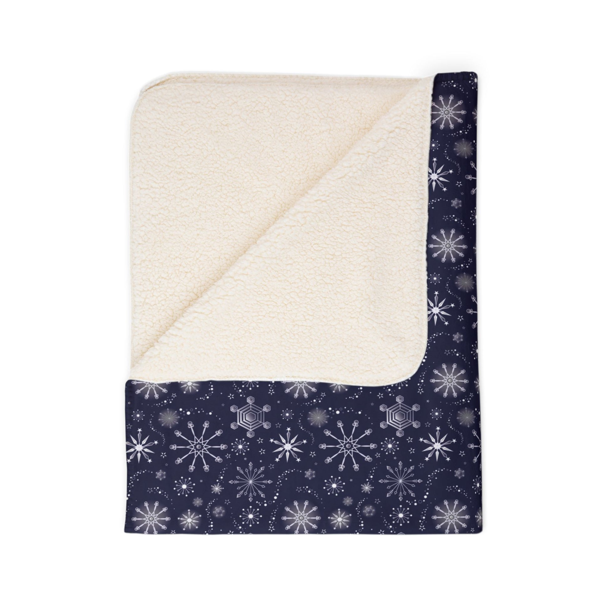 This is the beige 50" x 60" Winter Blizzard Sherpa Blanket. The blanket is folded. It is then revealed at the corner to show the inside sherpa and color. The background is white. The design are different types of snowflakes with different sizes of circles within each flake. The blanket is dark blue and the snowflakes and design are all white and spread throughout.