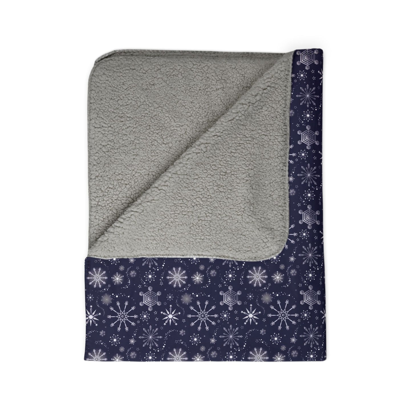 This is the grey 50" x 60" Winter Blizzard Sherpa Blanket. The blanket is folded. It is then revealed at the corner to show the inside sherpa and color. The background is white. The design are different types of snowflakes with different sizes of circles within each flake. The blanket is dark blue and the snowflakes and design are all white and spread throughout.